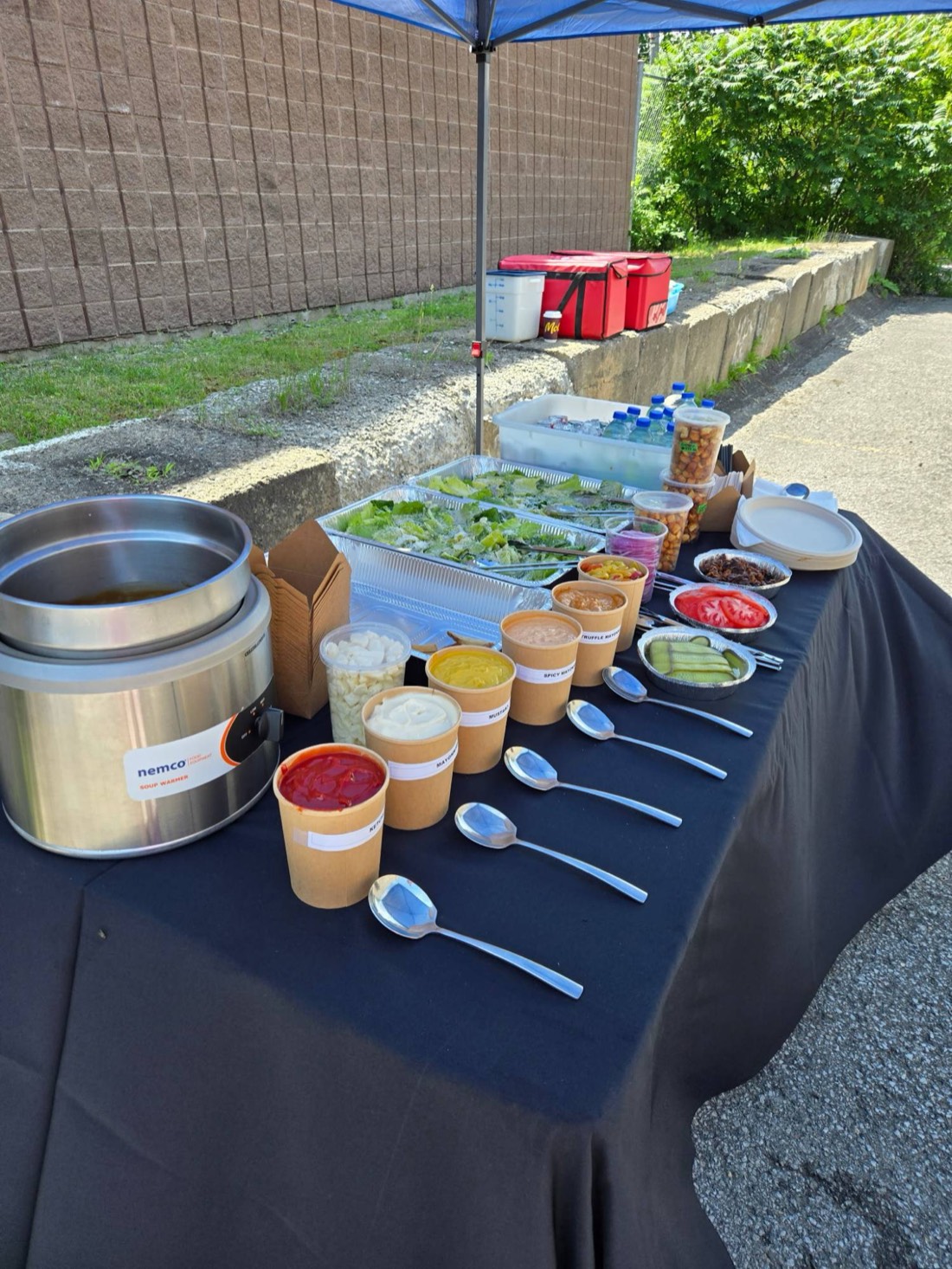 Our burger buffet set up outdoors under a tent, with salad trays, toppings and sauces in a row